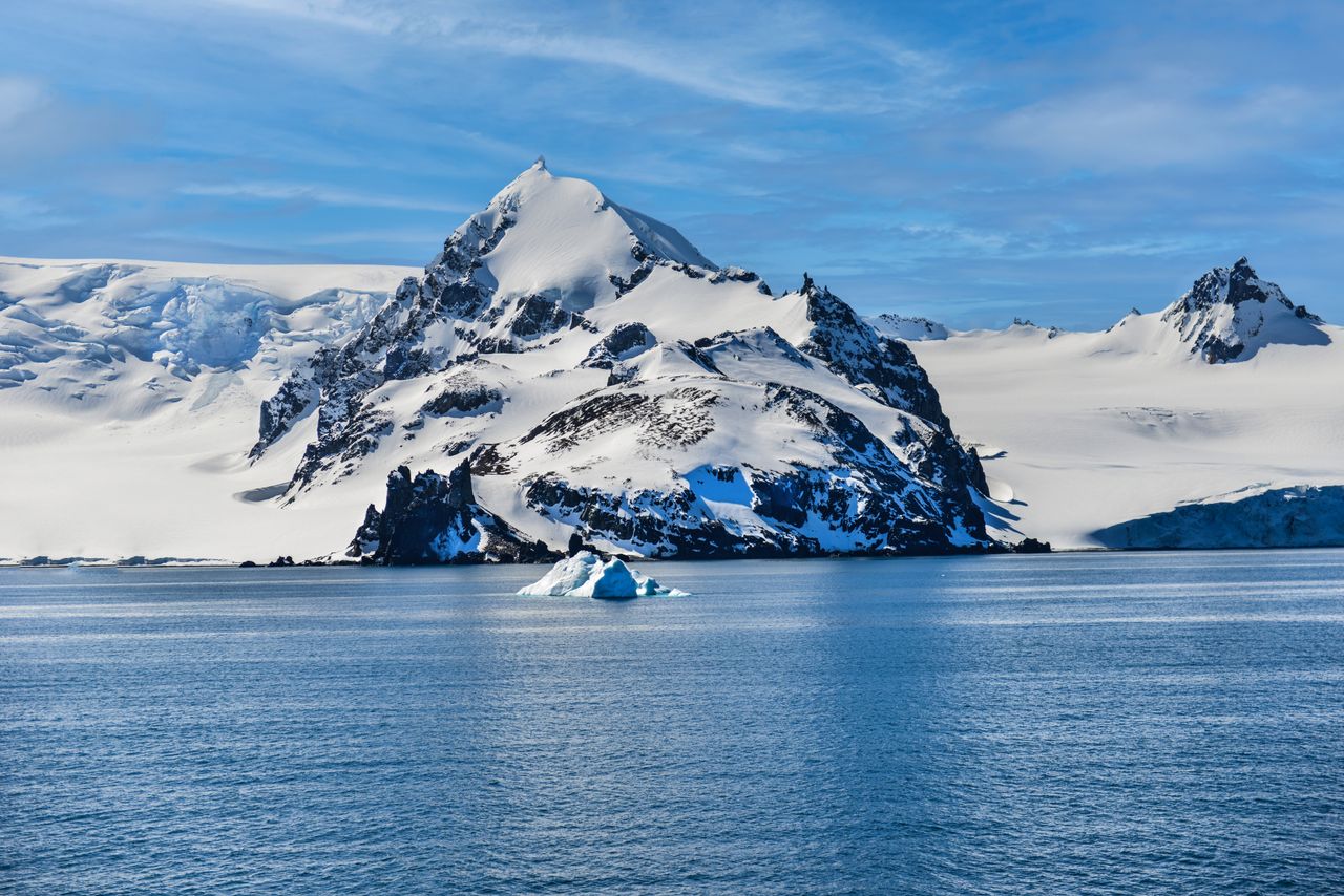 Services Stunning view of a snow-covered mountain and iceberg in Antarctica's icy waters.