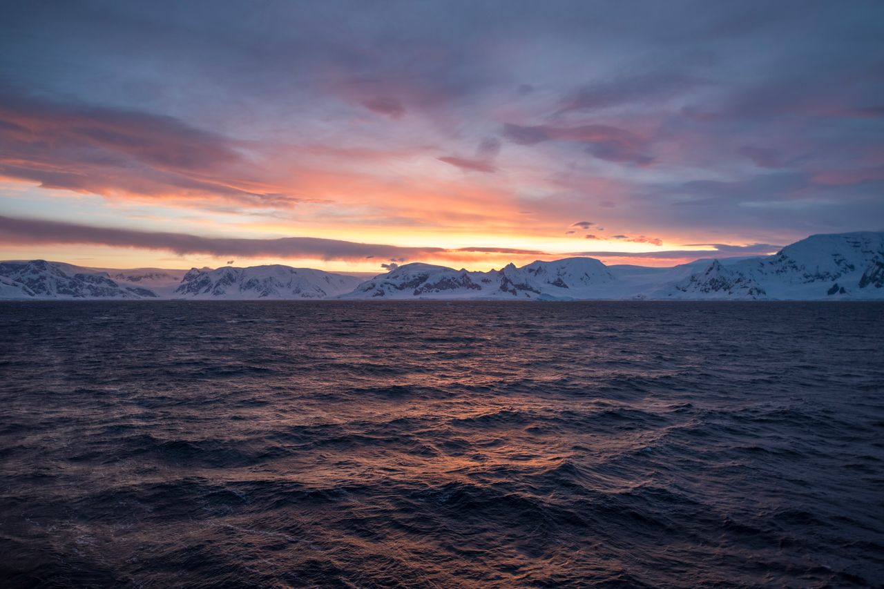 Services A breathtaking Antarctic sunrise with colorful skies reflecting over the ocean and snow-capped mountains.